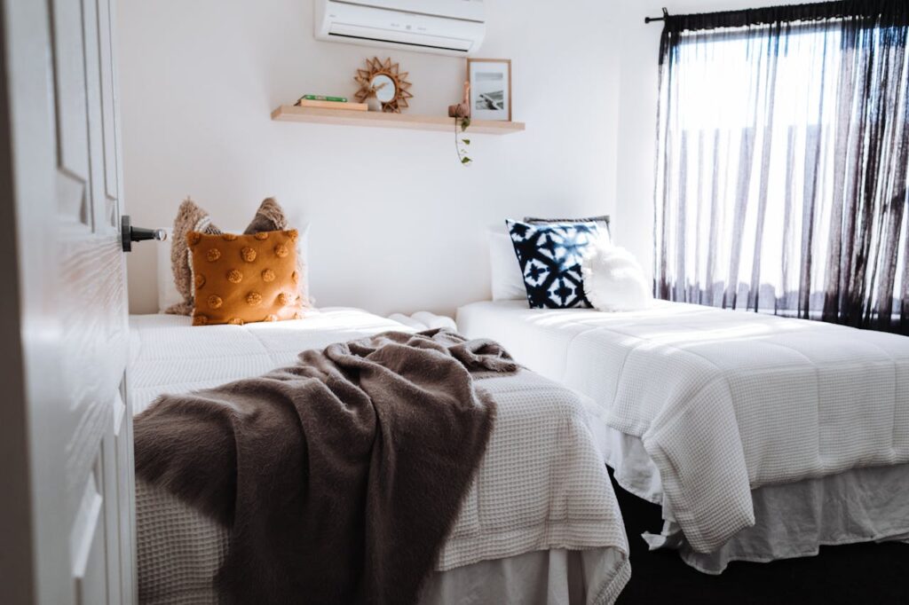 A beautifully styled twin bedroom with soft textures and natural sunlight.